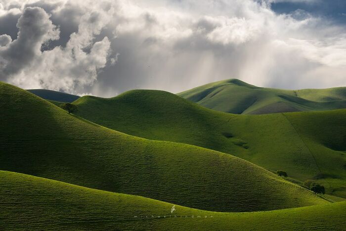 Green rolling hills under dramatic clouds, showcasing nature's textures.