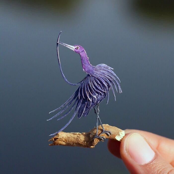 Miniature realistic paper art of a purple bird held on a fingertip, showcasing intricate details and craftsmanship.