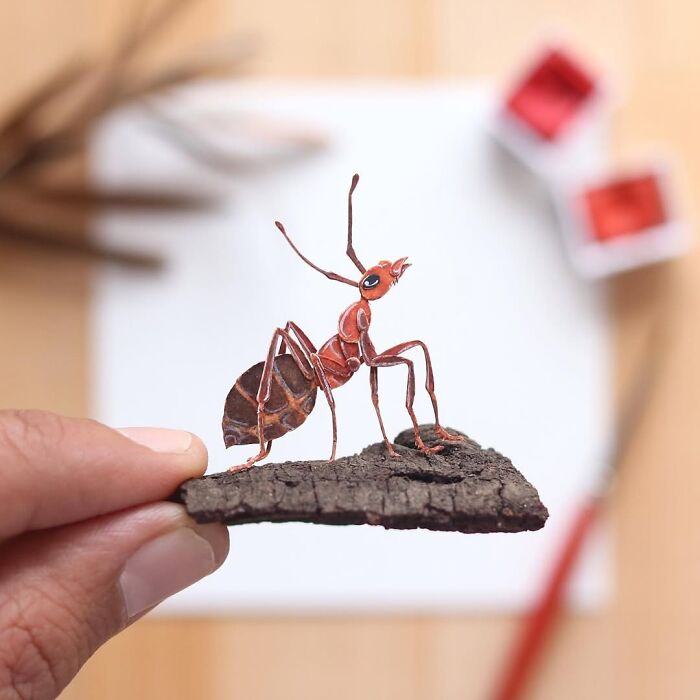 Miniature realistic paper art of an ant held by a hand, showcasing intricate details.
