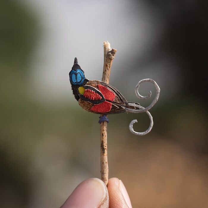 Miniature realistic paper art of a colorful bird on a twig.