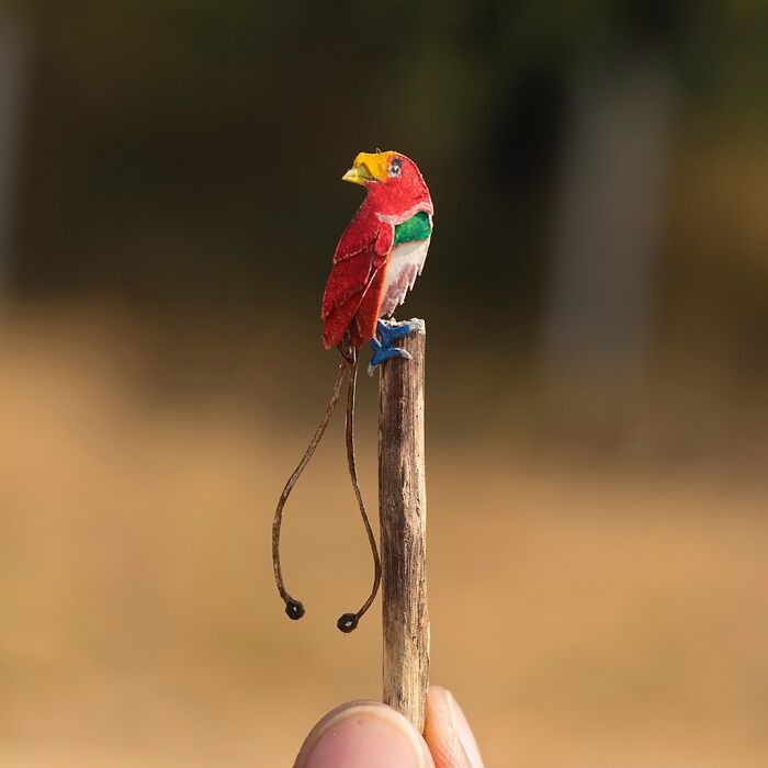 Miniature realistic paper art of a colorful bird perched on a twig, created to spark conservation conversation.