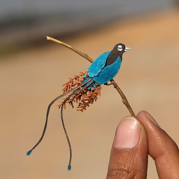 Miniature realistic paper art of a blue bird held on a small branch, created to spark conversation about conservation.