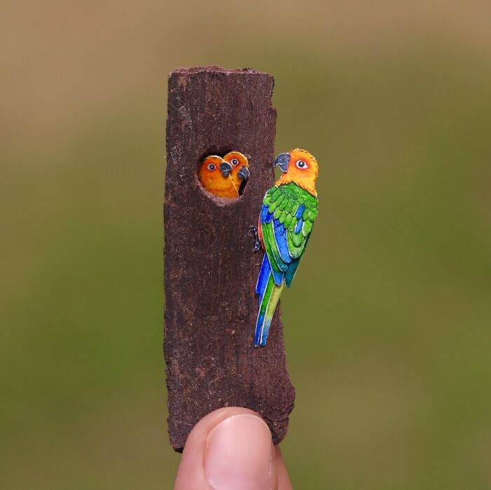 Miniature realistic paper art of colorful birds on wood, highlighting conservation themes.