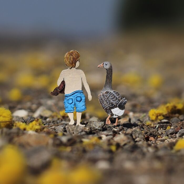 Miniature realistic paper art of a boy and goose walking together on a pebbled path, highlighting animal conservation.