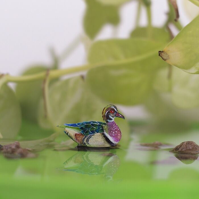 Miniature realistic paper art duck by artists, surrounded by greenery, showcasing conservation through animal art.