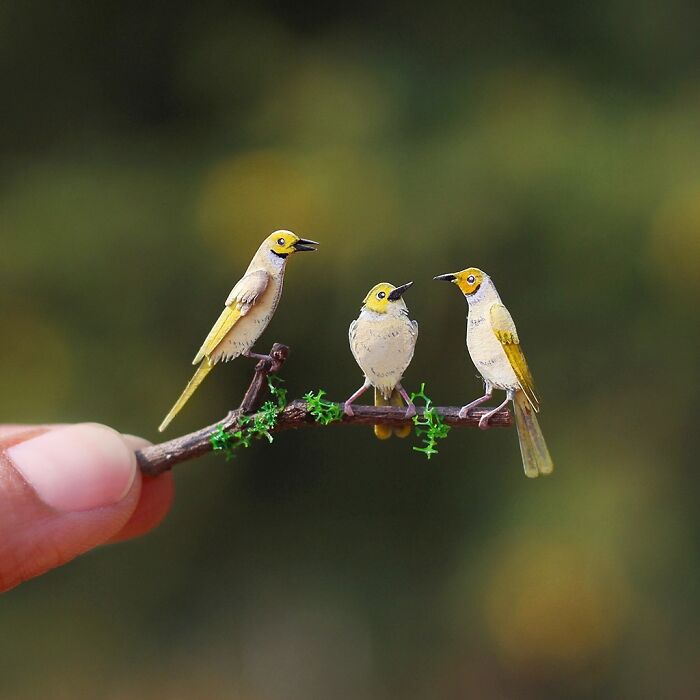 Miniature realistic paper art of three birds on a branch, showcasing artistic detail in animal conservation theme.