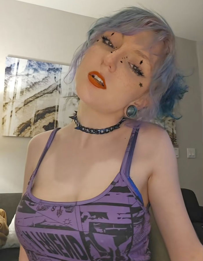 Person with colorful hair and tattoos in an open relationship setting, wearing a purple patterned top. Person with colorful hair and tattoos in an open relationship setting, wearing a purple patterned top.