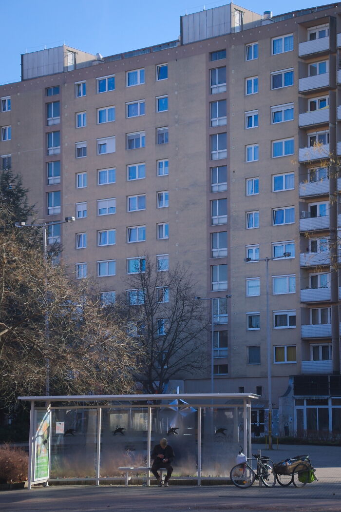 Hungary panel building with a bus stop in front, featuring a person sitting and a bicycle nearby.