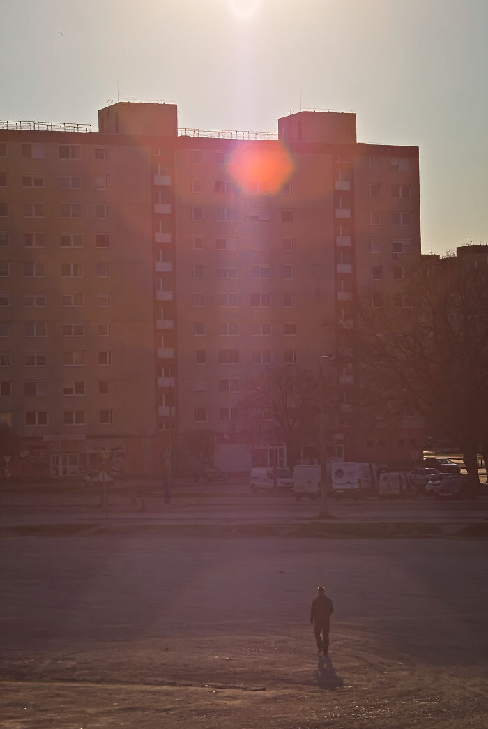 Sunlit view of a panel building in Hungary with a solitary figure walking across an empty space.
