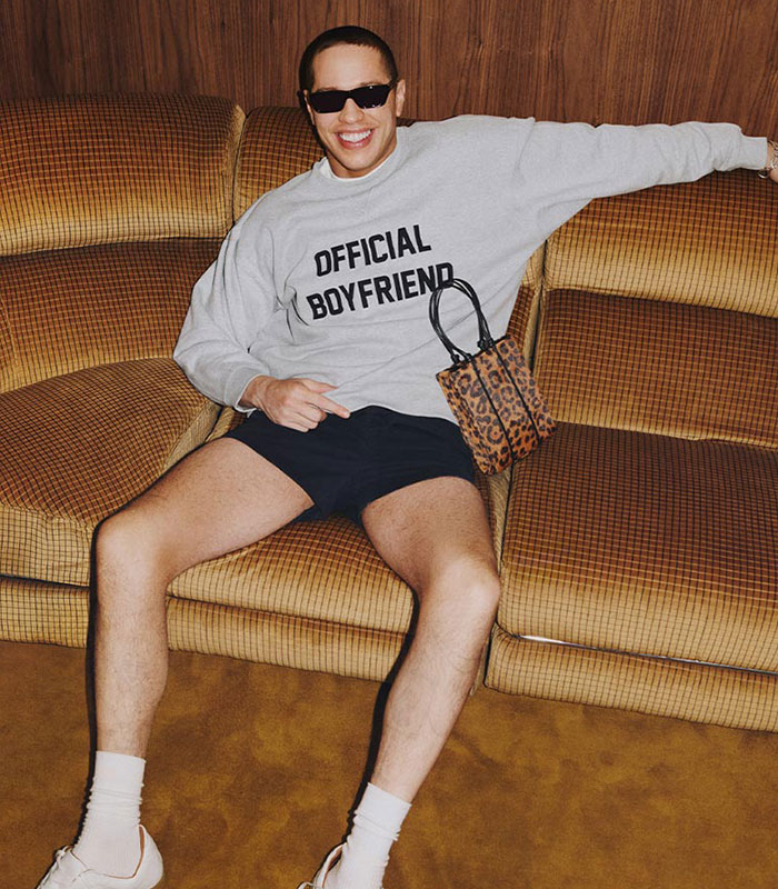 Pete Davidson in a "Official Boyfriend" shirt, sunglasses, and shorts, sitting on a couch, showcasing Reformation campaign style.