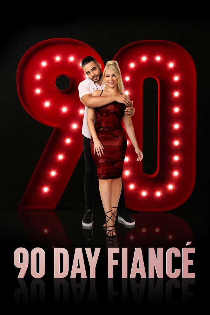 Couple posing in front of large illuminated "90" sign for TV show 90 Day Fiancé.