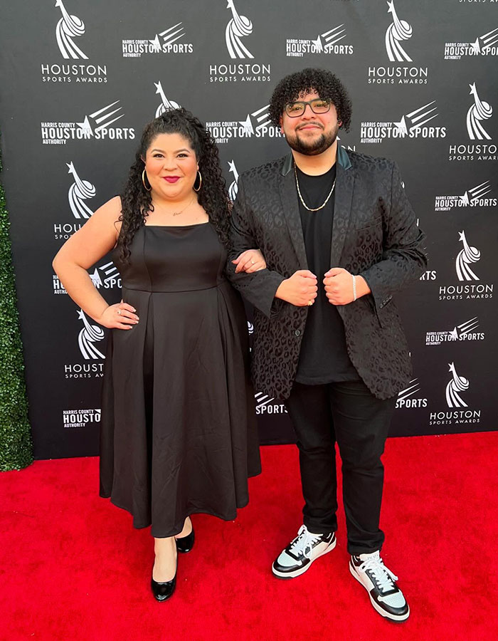 Red carpet appearance at Houston Sports Awards with two people, one in a black dress, the other in a patterned black jacket.