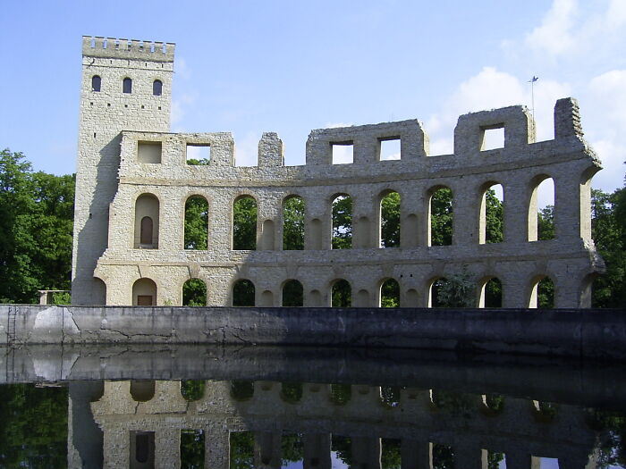 Ruined building reflected in water, displaying beautiful yet useless architecture against a clear sky.