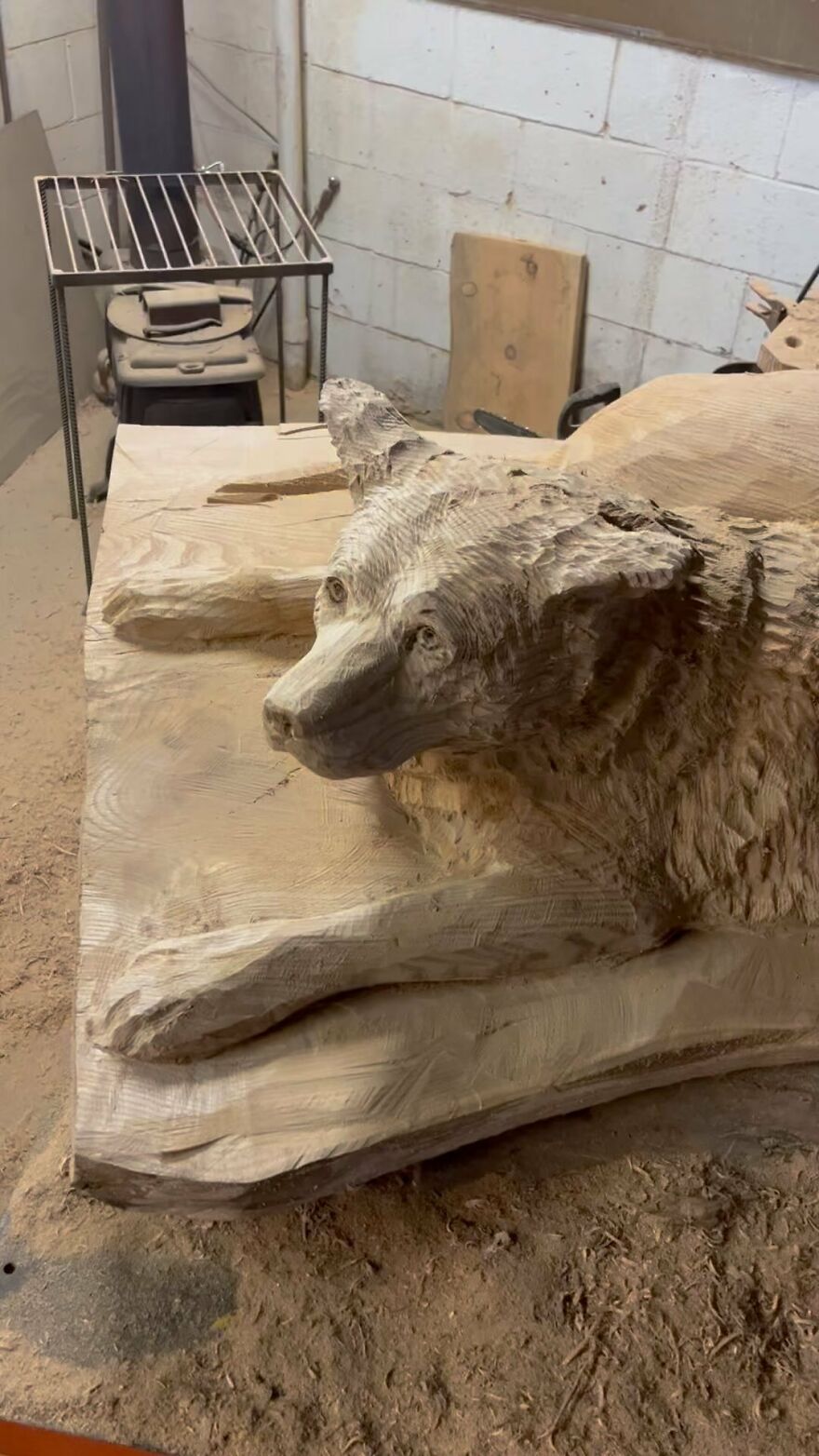 Chainsaw artist crafts a detailed wooden sculpture of a reclining animal in a workshop setting.
