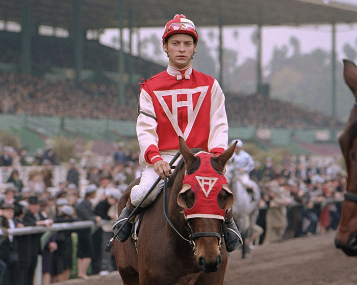 Jockey in red and white attire riding a horse at a racetrack, illustrating a time Hollywood got history wrong.