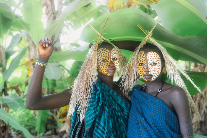 Ethiopian people in traditional face paint and attire, standing amidst lush green foliage.