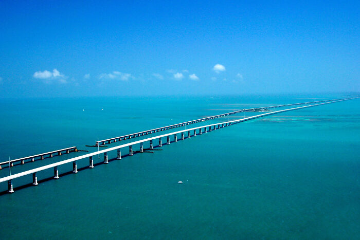 Aerial view of a long highway over the ocean, part of legendary American road routes, under a clear blue sky.