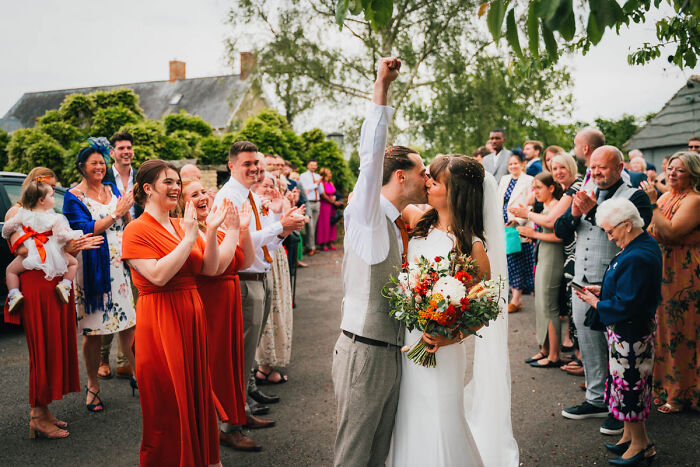 Bride and groom kiss joyfully amid cheering guests, showcasing one of the best wedding photographs.