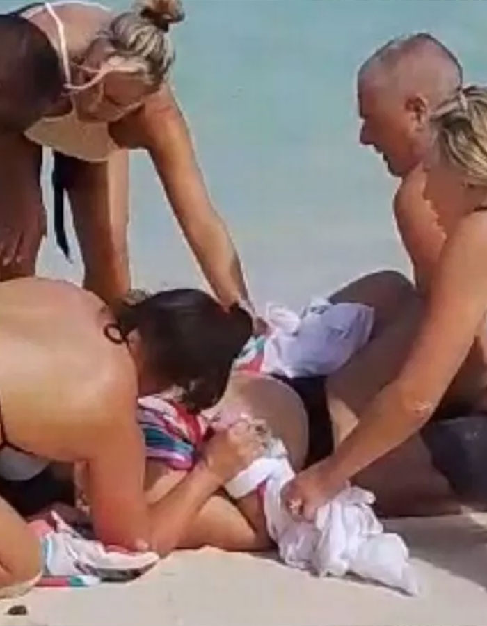 People tending to a woman on a beach after a shark attack incident involving shark engagement for a photo. People tending to a woman on a beach after a shark attack incident involving shark engagement for a photo.