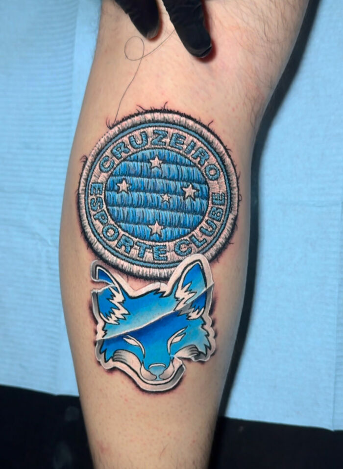 Realistic embroidery tattoo of a blue and white fox with "Cruzeiro Esporte Clube" text on a person's arm.