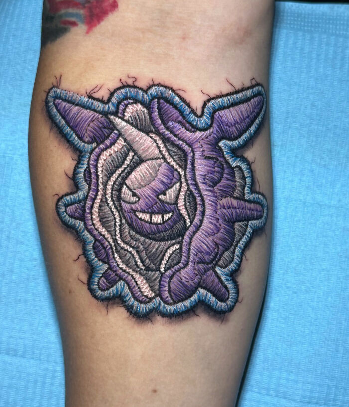 Realistic embroidery tattoo of a purple cloyster on a person's arm, showcasing intricate stitch-like detail.