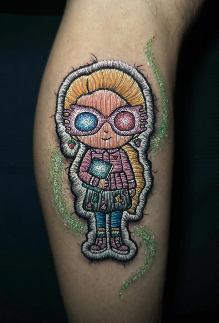 Realistic embroidery tattoo of a doll on skin, showcasing colorful thread-like details.