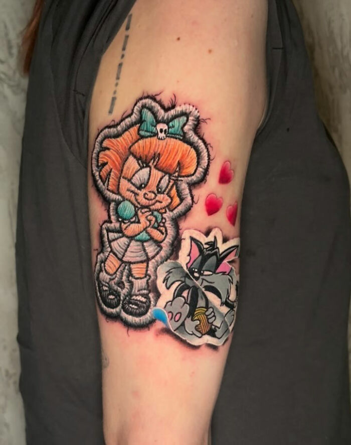 Realistic embroidery tattoo with cartoon characters and red hearts on upper arm.