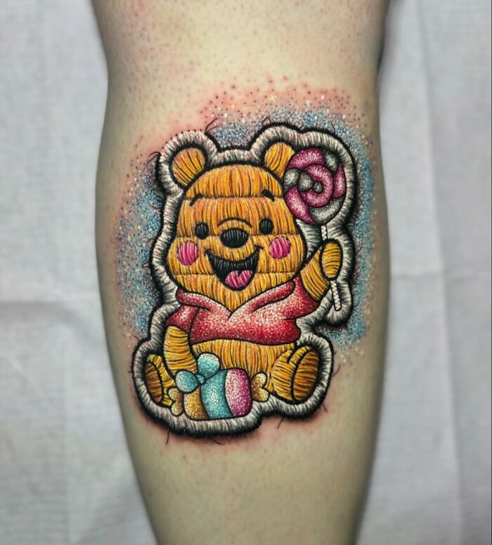 Realistic embroidery tattoo of a bear holding a lollipop, showcasing vibrant colors and intricate details.