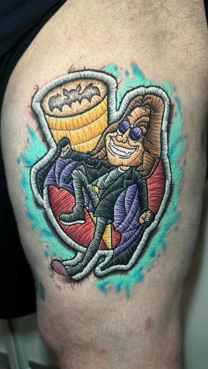 Realistic embroidery tattoo of a character with sunglasses and bat detail, vibrant colors on skin.