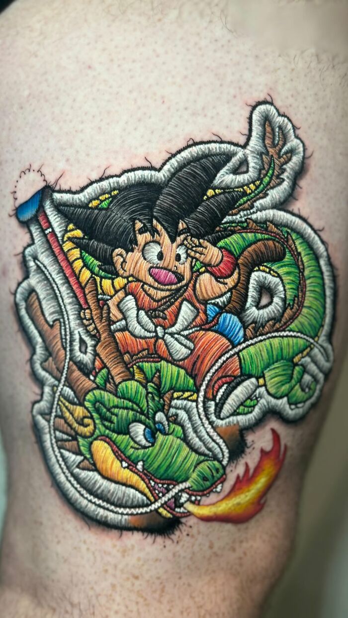 Realistic embroidery tattoo with vibrant colors, featuring a cartoon character and dragon on a person's arm.