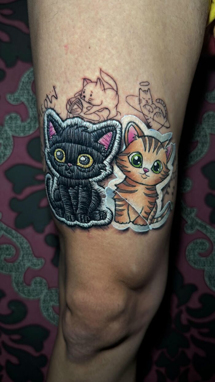 Realistic embroidery tattoo of two cats on a leg, featuring detailed stitching and vibrant colors.