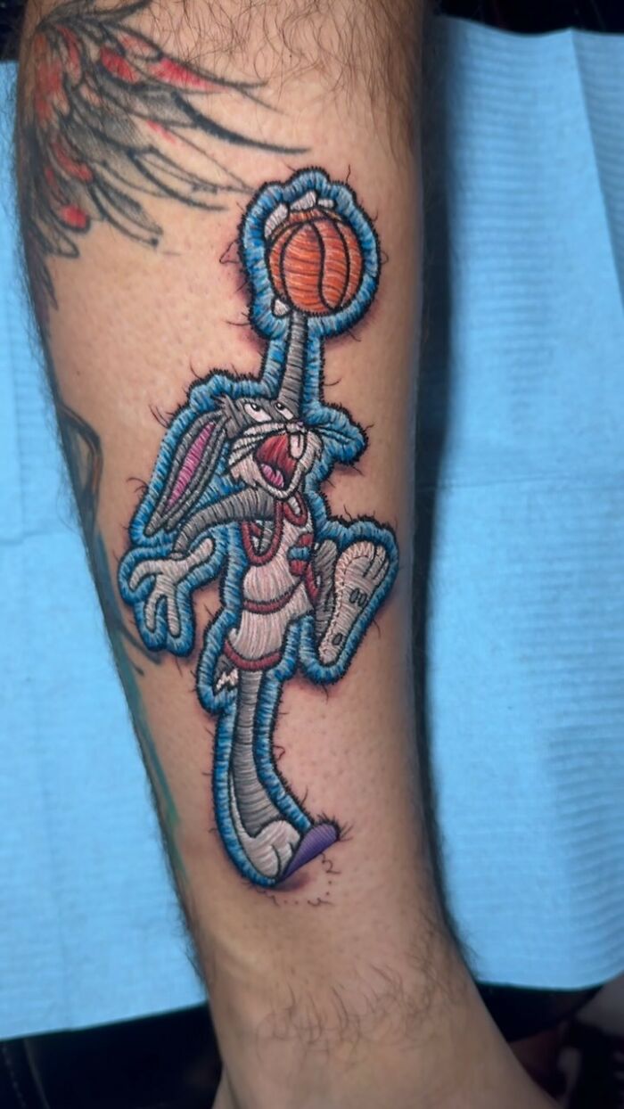Realistic embroidery tattoo of cartoon character holding a basketball on a person's arm.