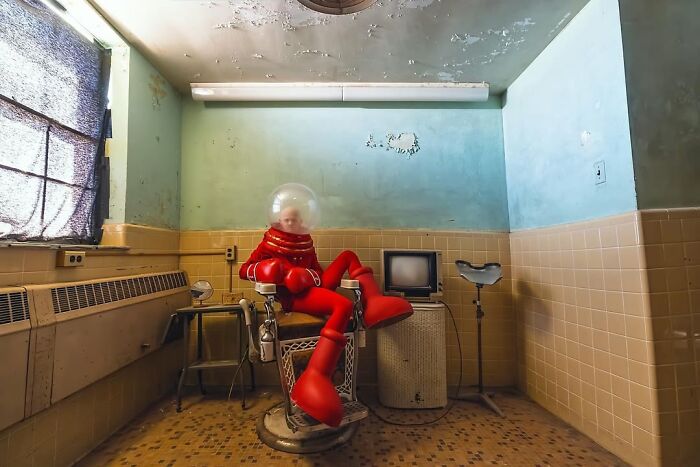 Model in a futuristic red suit seated in a vintage room with an old TV and retro decor.