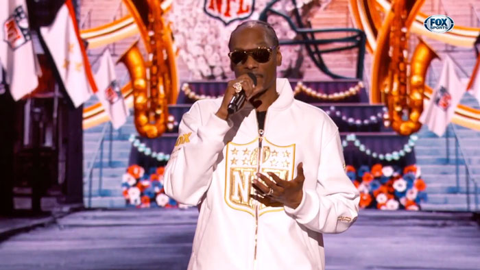Snoop Dogg speaking on stage in a white NFL jacket, joking about an age gap, gaining viral attention.