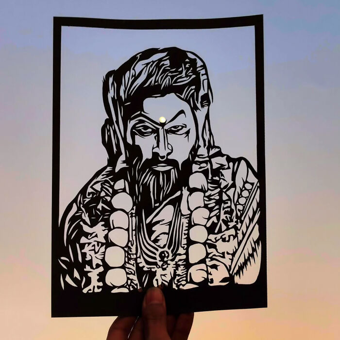 Paper-cutting artist creation featuring an intricate portrait silhouette held against a twilight sky.