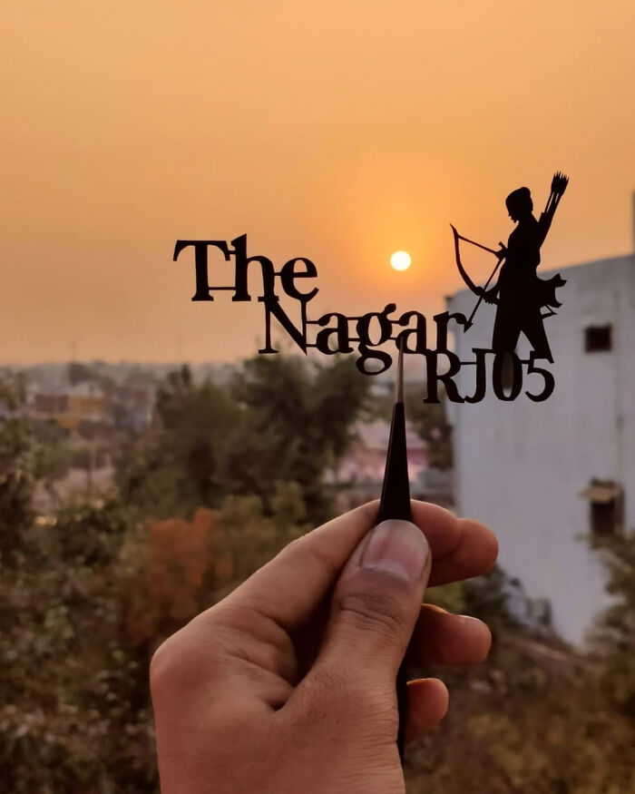 Professional paper-cutting artist holding a detailed cutout against a sunset backdrop.