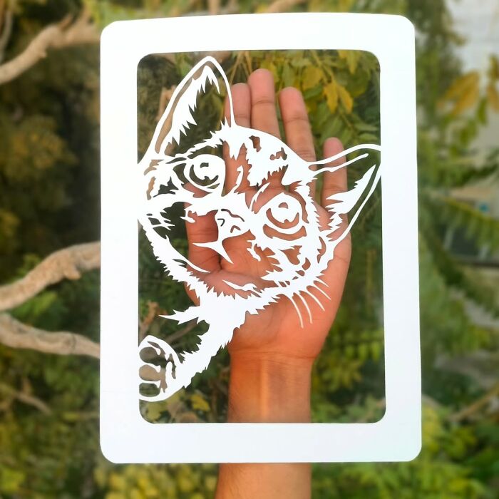 Paper-cutting art of a cute cat held against a leafy background by a professional artist.