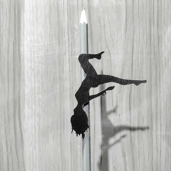 Paper-cutting art of a dancer silhouette balancing on a pencil against a wooden background.