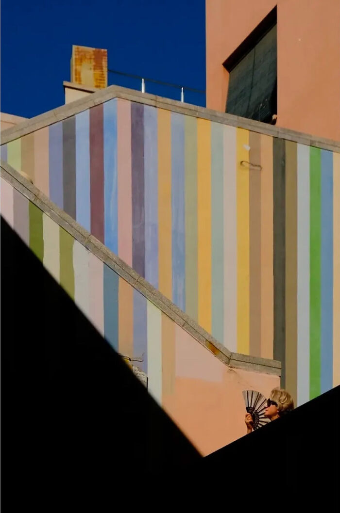 Abstract street photograph featuring a colorful striped wall and a person holding a fan, capturing urban aesthetics.