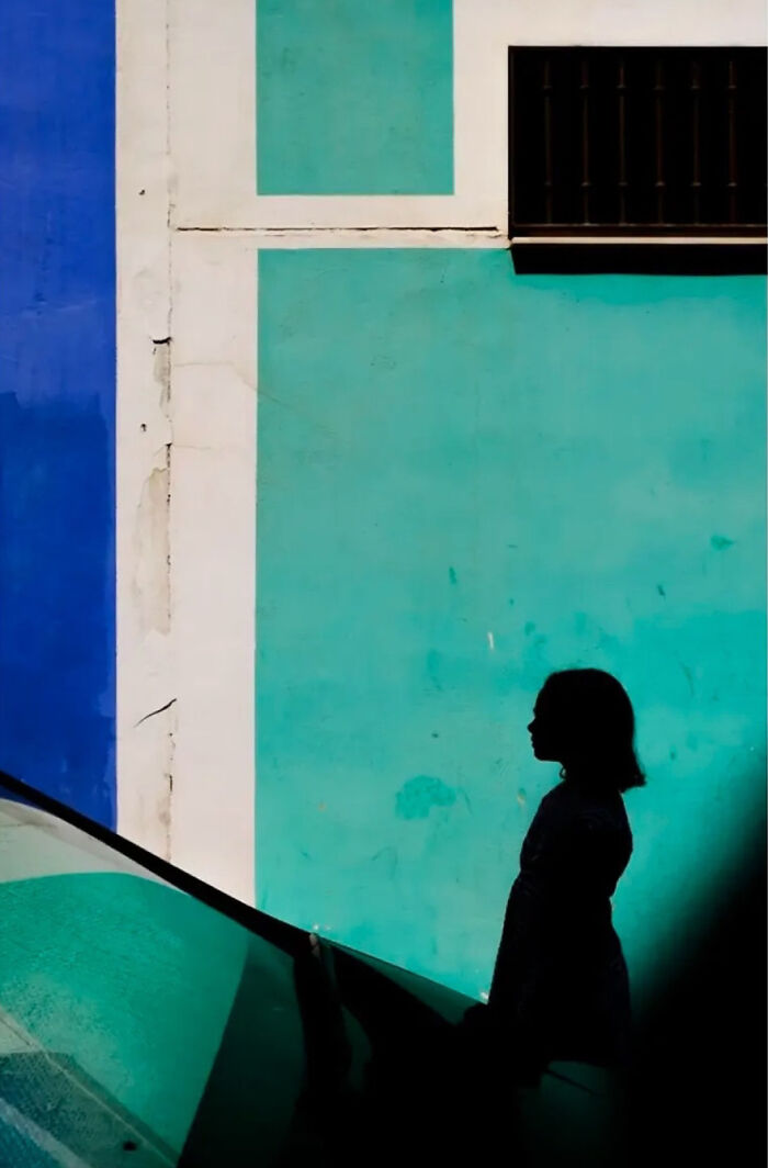 Silhouette of a person against a vibrant blue and green wall, showcasing abstract street photography by Andrea Pozzoni.
