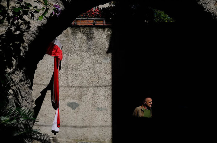 Abstract street photograph by Andrea Pozzoni showing a person in a shadowed archway, contrasted with vibrant red and white cloth.