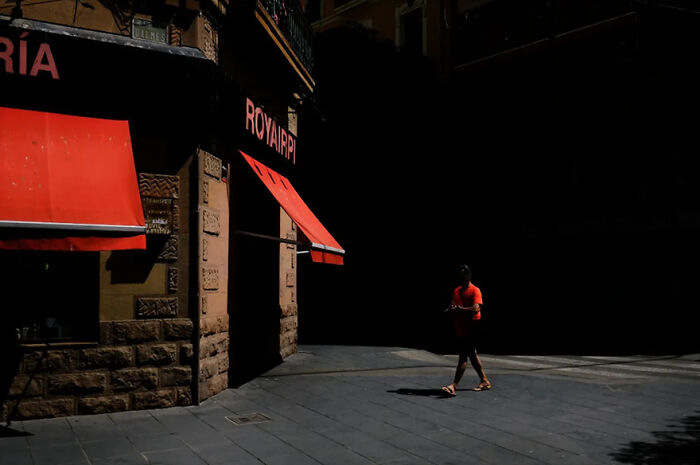Abstract street photograph showing a person in a red shirt walking past a building with red awnings.