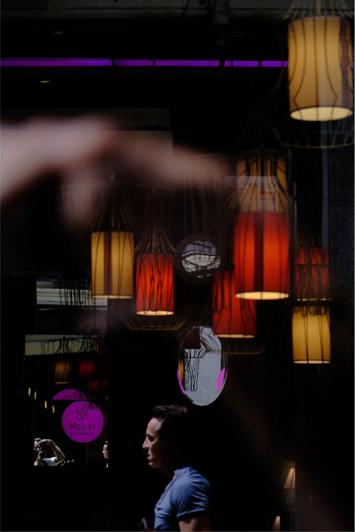 Abstract street photograph by Andrea Pozzoni featuring a man and reflections of colorful lamps on a dark background.