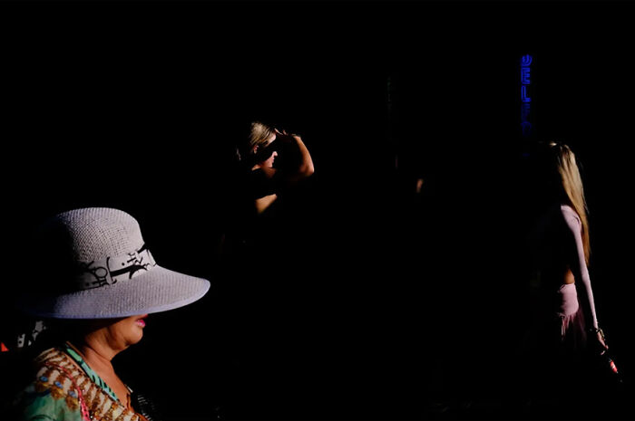 Abstract street photograph featuring three people in contrasting light and shadows.