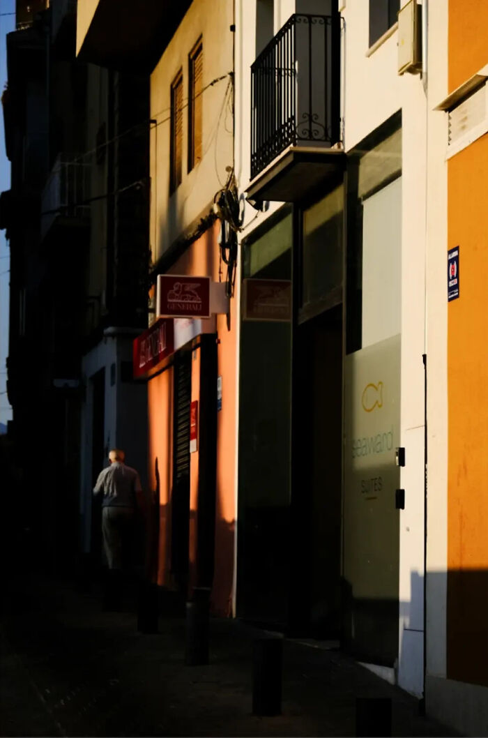 Abstract street photograph by Andrea Pozzoni, depicting a man walking down a dimly lit alley with vibrant wall shadows.