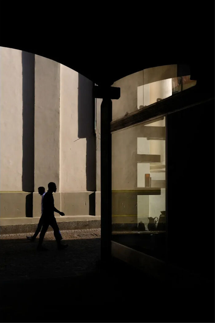 Silhouettes walking beneath an archway, capturing abstract street photography by Andrea Pozzoni.