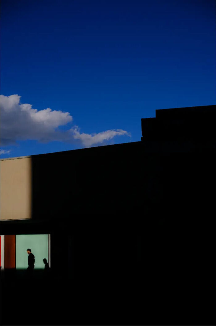 Abstract street photo with silhouettes against a stark blue sky and shadowed architecture.