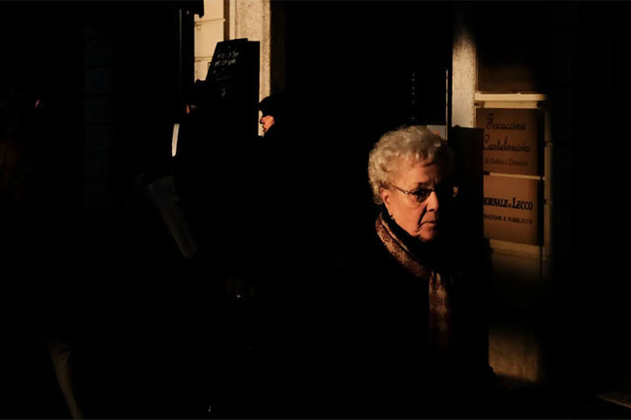 Elderly woman in shadows, highlighting abstract street photography by Andrea Pozzoni.