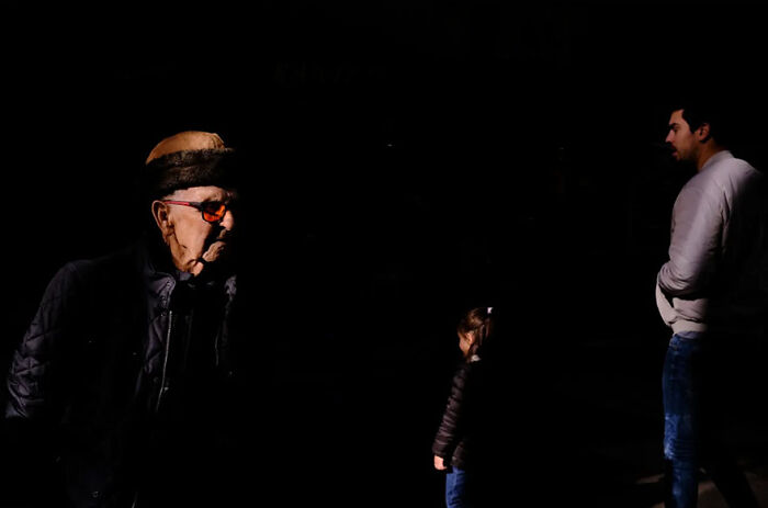 Abstract street photograph depicting a man, a child, and a woman in shadows, creating a striking contrast in lighting.