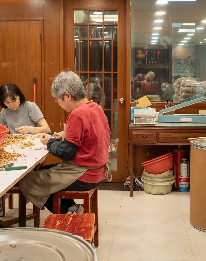 People working in a room while a cat sits by a wooden door, captured in a city scene by Marcel Heijnen.